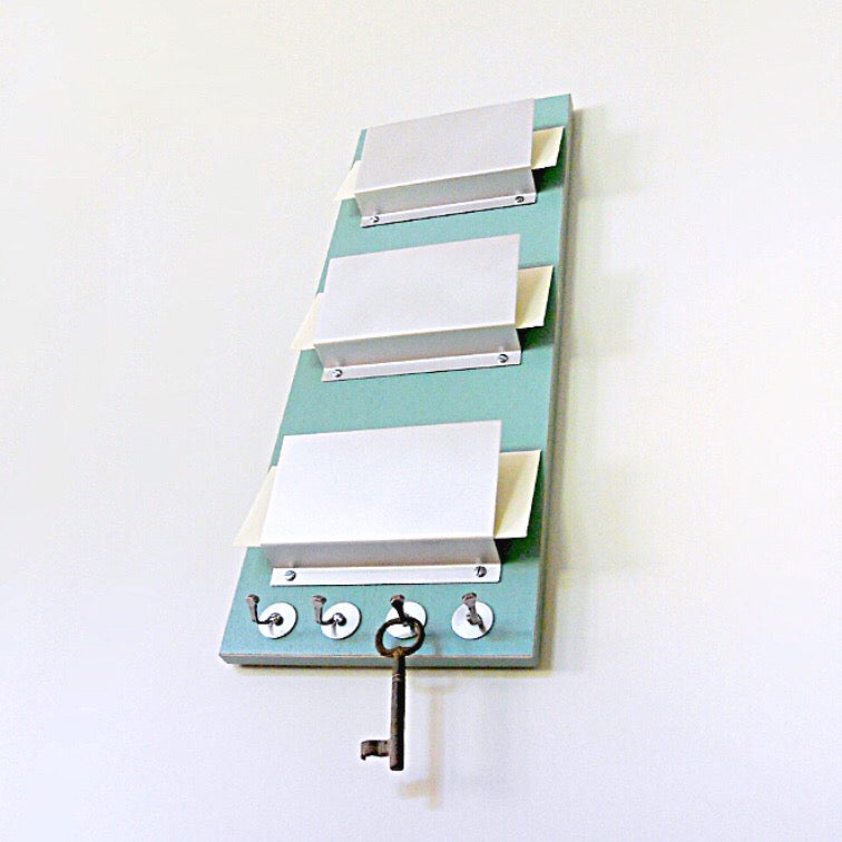 Mail holder piece titled RUE mounted on the wall. This piece includes three holders and key hooks at the bottom. The color of the piece is Soda.
